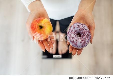 Diet. Woman Measuring Body Weight On Weighing Scale Holding Donut and apple. Sweets Are Unhealthy 48372676