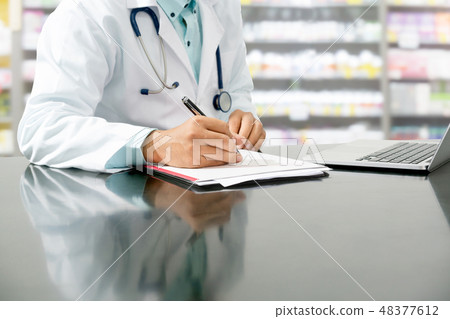 Pharmacist writes on documents at pharmacy. Pharmacist writes on documents at pharmacy. 48377612