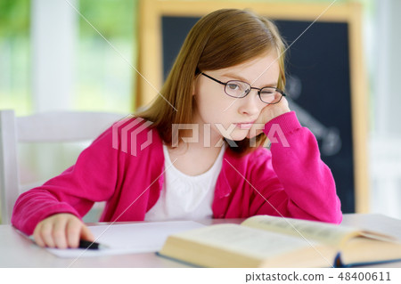 Stressed and tired schoolgirl studying with a pile of books on her desk 48400611