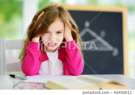 Stressed and tired schoolgirl studying with a pile of books on her desk 48400612