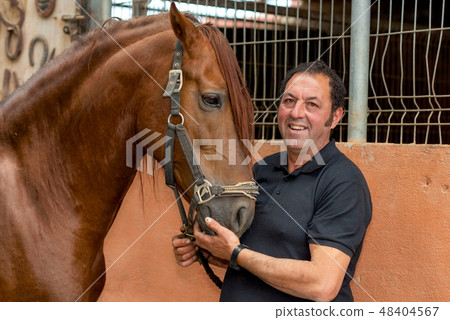 Portrait of a handsome man with his horse standing at the stable