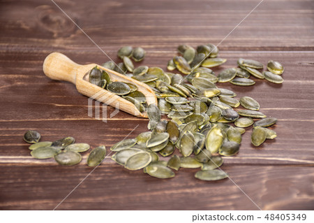 Hulled pumpkin seeds on brown wood Hulled pumpkin seeds on brown wood 48405349