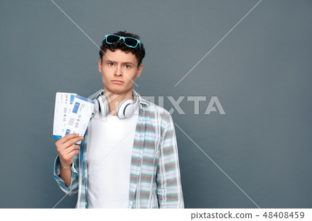 Man isolated on gray wall tourism concept standing holding two tickets looking camera upset Man isolated on gray wall tourism concept standing holding two tickets looking camera upset 48408459