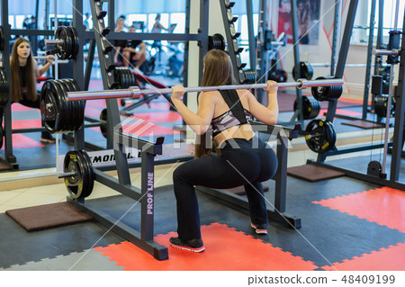 Beautiful girl crouches with a barbell on the 48409199