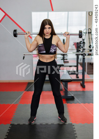 Beautiful girl crouches with a barbell on the Beautiful girl crouches with a barbell on the 48409243