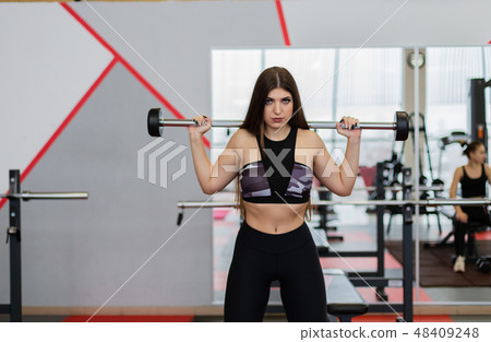 Beautiful girl crouches with a barbell on the Beautiful girl crouches with a barbell on the 48409248