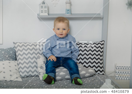 A little boy sits in on pillows in clothes. A little boy sits in on pillows in clothes. 48410879