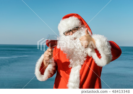Fat man in glasses dressed as Santa drinking wine Fat man in glasses dressed as Santa drinking wine 48413348