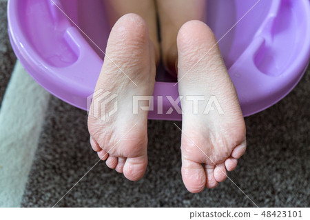 Child girl feet sticking out of the bathtub. The skin on feets, toes wrinkles. 48423101