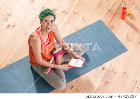 Beaming freelancer sitting with legs crossed on blue sport mat Beaming freelancer sitting with legs crossed on blue sport mat 48429297