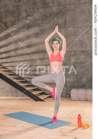 Green-haired woman wearing pink sneakers standing in tree pose 48429404