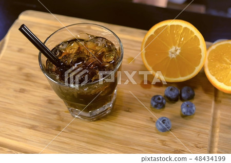 Alcohol cocktail on the rocks glass with orange, ice and blueberry on the table, Side view. Alcohol cocktail on the rocks glass with orange, ice and blueberry on the table, Side view. 48434199