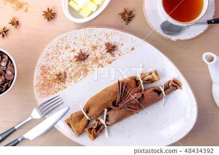 Chocolate russian pancakes, blini with curd filling on the plate. Served with a cup of tea and 48434392