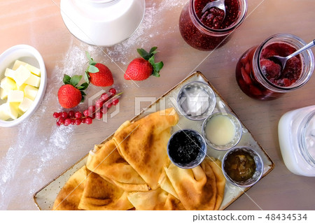 Traditional russian pancakes, blini. Served with jams, sour cream, milk and strawberry on the plate 48434534