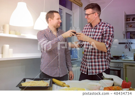 Men gay clink glasses, drink wine and cook pizza in the kitchen. Gay family life. Men gay clink glasses, drink wine and cook pizza in the kitchen. Gay family life. 48434734