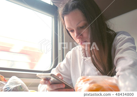 Tired woman is reading a book in smartphone travelling on a long distance train. Tired woman is reading a book in smartphone travelling on a long distance train. 48434800