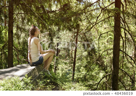 Dreaming beautiful girl sitting on a stone Dreaming beautiful girl sitting on a stone 48436019