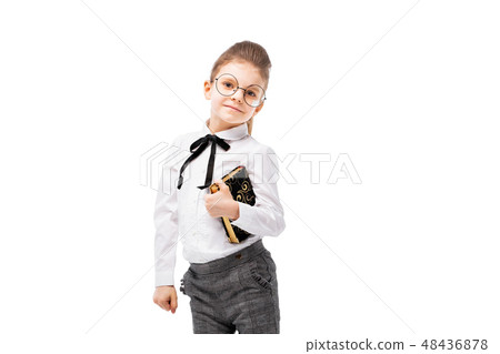 Beautiful little girl in white shirt and gray pants standing near white wall and posing like model 48436878