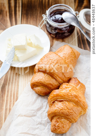 two croissants, butter and jam on a wooden table. 48448637