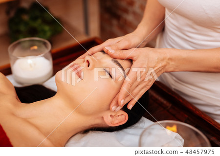 Experienced masseuse in white t-shirt making relaxing massage for face 48457975