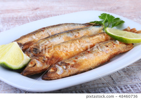 Deep frying small fish capelin and sliced lemon on white plate. Good snack to beer. Deep frying small fish capelin and sliced lemon on white plate. Good snack to beer. 48460736