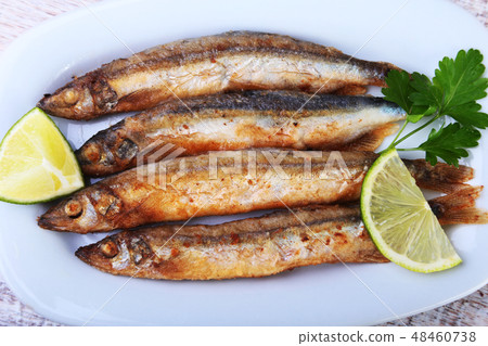 Deep frying small fish capelin and sliced lemon on white plate. Good snack to beer. Deep frying small fish capelin and sliced lemon on white plate. Good snack to beer. 48460738