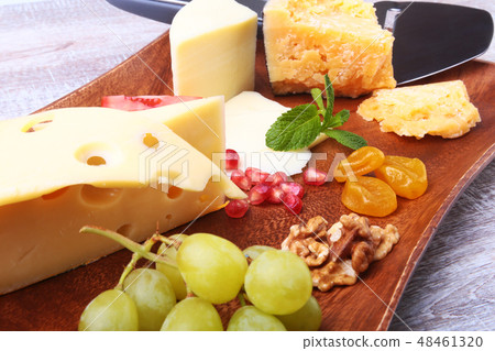 Assortment of cheese with fruits, grapes, nuts and cheese knife on a wooden serving tray. Assortment of cheese with fruits, grapes, nuts and cheese knife on a wooden serving tray. 48461320