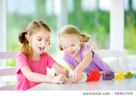 Two sisters having fun with modeling clay Two sisters having fun with modeling clay 48463564