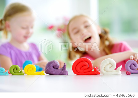 Two sisters having fun with modeling clay Two sisters having fun with modeling clay 48463566