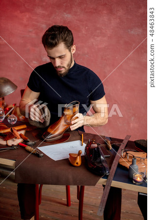 serious workman giving leather boots a high polish in workshop 48463843