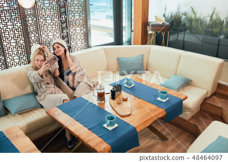 Relaxed diverse friends in bathrobes sitting at lounge zone of bathhouse 48464097