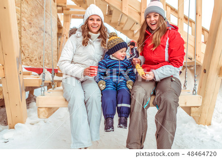 Happy family mom with girlfriend, little son 3-6 years old. Rest in city winter on wooden swing Happy family mom with girlfriend, little son 3-6 years old. Rest in city winter on wooden swing 48464720
