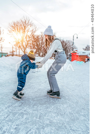 Young woman mom skates with her young son, a boy of 3-5 years. In the winter in the city on the rink 48464810