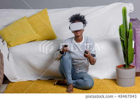 African woman watching video using VR glasses with remote control at home. African woman watching video using VR glasses with remote control at home. 48467043