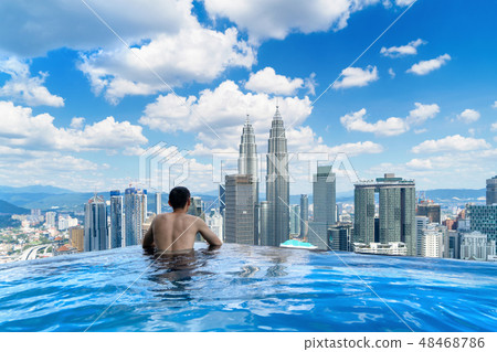 Back of tourist in a swimming pool on rooftop with Kuala Lumpur Back of tourist in a swimming pool on rooftop with Kuala Lumpur 48468786