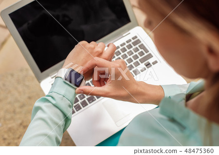 Young woman sitting on stairs working on laptop checking time on watch close-up top view 48475360