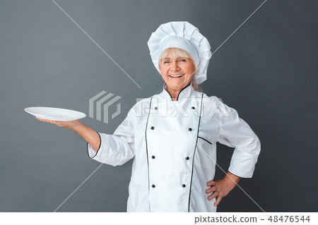 Senior woman chef studio standing isolated on gray holding plate looking camera laughing cheerful 48476544