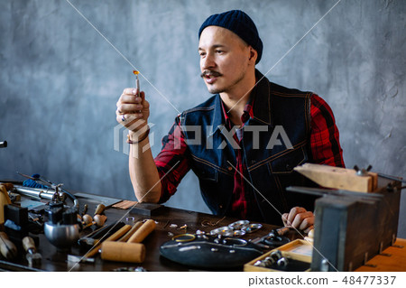 young attractive artisan checking the quality of amber in the jewellery shop young attractive artisan checking the quality of amber in the jewellery shop 48477337