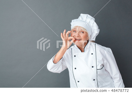 Senior woman chef studio standing isolated on gray showing ok sign looking camera playful 48478772