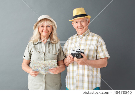 Senior tourists in beach hats studio standing isolated on gray holding camera and map cheerful 48478840