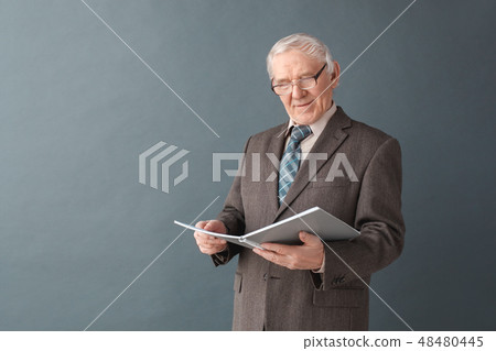 Senior man teacher wearing glasses studio standing isolated on gray reading journal concentrated 48480445