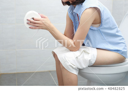 Woman in bath towel sitting on toilet bowl. 48482825