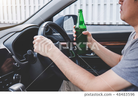 Young asian man drives a car with drunk a bottle of beer behind 48483596