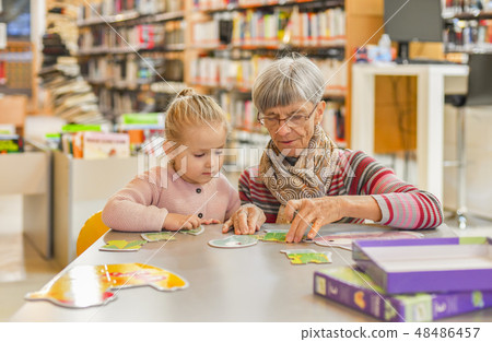 Granddaughter and grandmother put together a puzzle in the city library Granddaughter and grandmother put together a puzzle in the city library 48486457