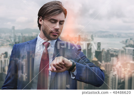 Confidence and punctuality. Busy young businessman in suit looking at his watch while standing 48486620