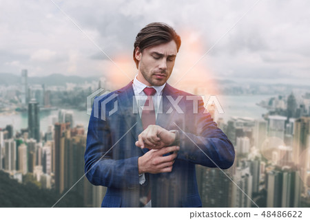 What time is it? Busy and confident businessman in suit looking at his watch while standing against 48486622