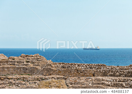 ruins of an ancient amphitheater and a cargo ship sailing in the mediterranean sea ruins of an ancient amphitheater and a cargo ship sailing in the mediterranean sea 48488137