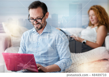 Smiling clever man working while a cheerful woman sitting behind him 48489710