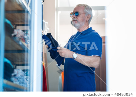 Concentrated elderly man thinking about trying new T-shirt on 48493034