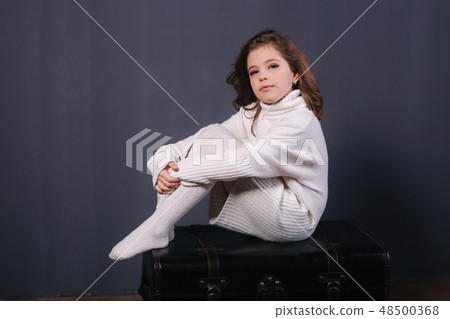 Little beautiful girl with brown hair in a white sweater. Studio. A princess poses for a Little beautiful girl with brown hair in a white sweater. Studio. A princess poses for a 48500368
